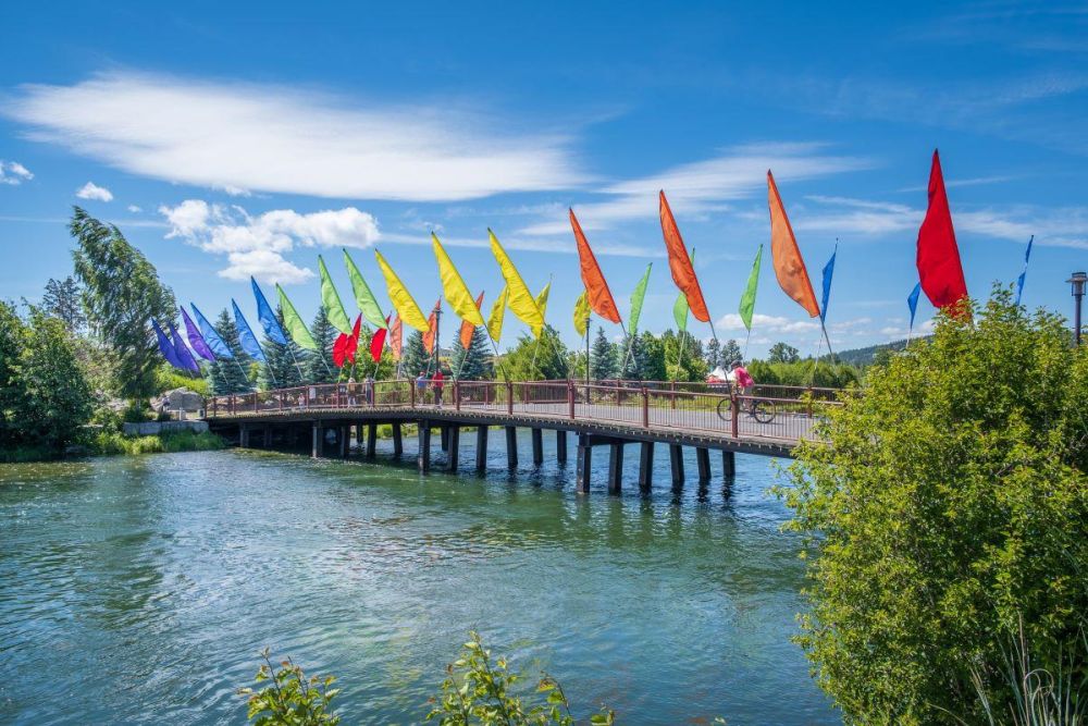 Colorful flags line a pedestrian bridge over the Deschutes River in the Old Mill District of Bend.