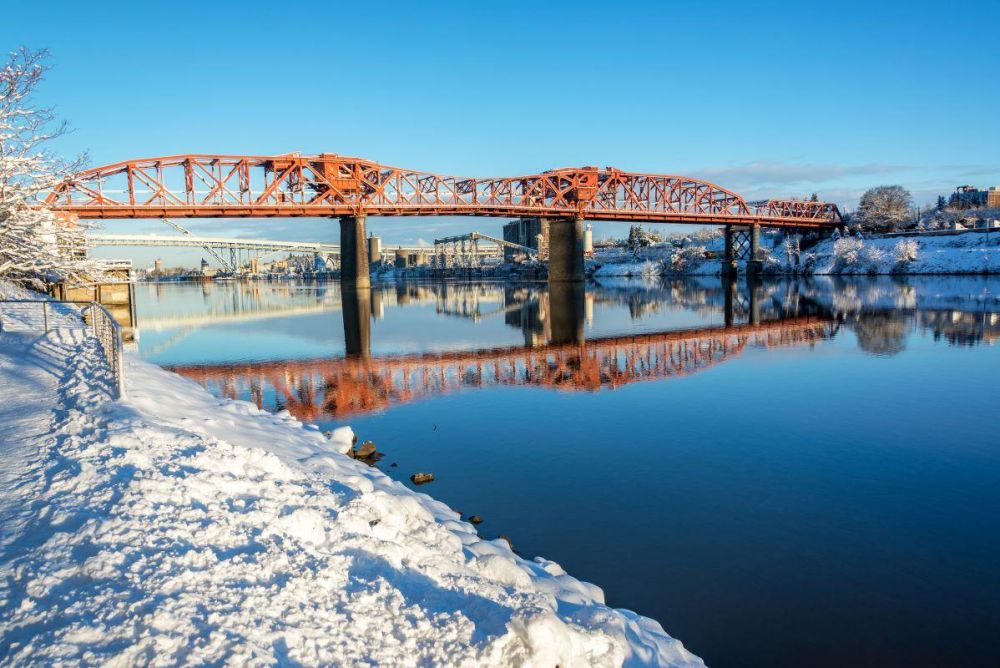 A reflection of Broadway Bridge shimmers in the Willamette River as snow lines the banks in Portland.