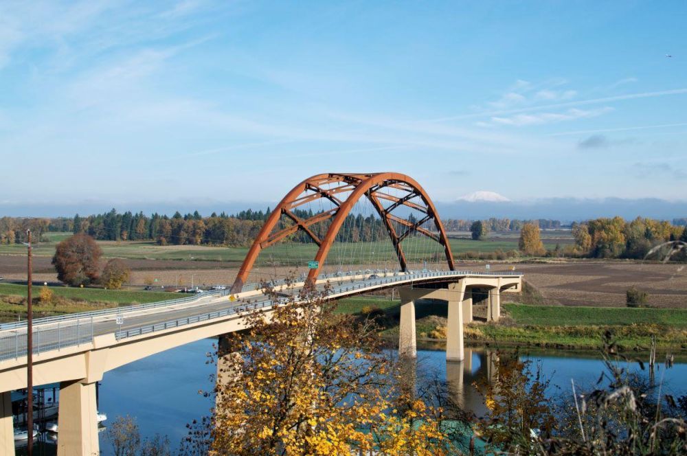 The red arches of Sauvie Island Bridge cross the Multnomah Channel of the Willamette River near Portland. In the background is snow-capped Mt. St. Helens.