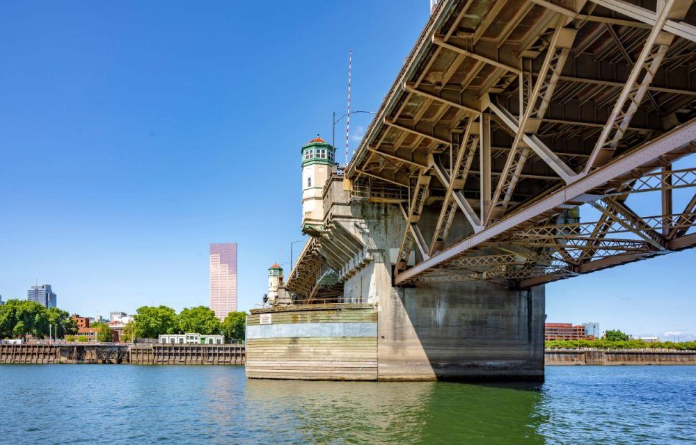 The underside of the Burnside Bridge in Portland is seen above the green-blue waters of the Willamette River.