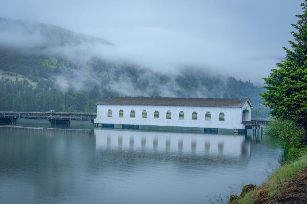 The Lowell covered bridge stands above the Dexter Reservoir outside Lowell. Ragged clouds obscure tree-covered hillsides.