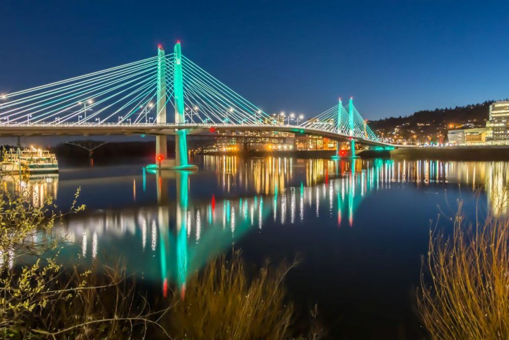 Tilikum Crossing glows with green light at night over the Willamette River.